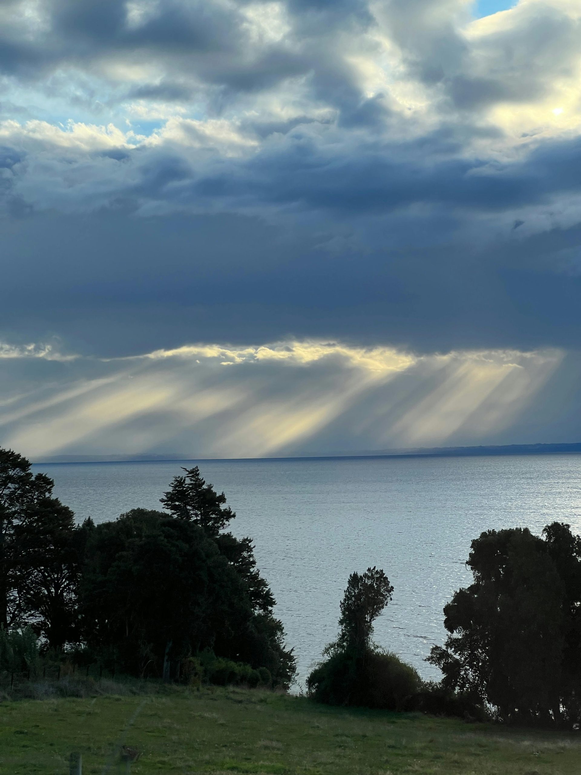 Captivating view of sun rays piercing through clouds over a serene lake in Puerto Varas, Chile.